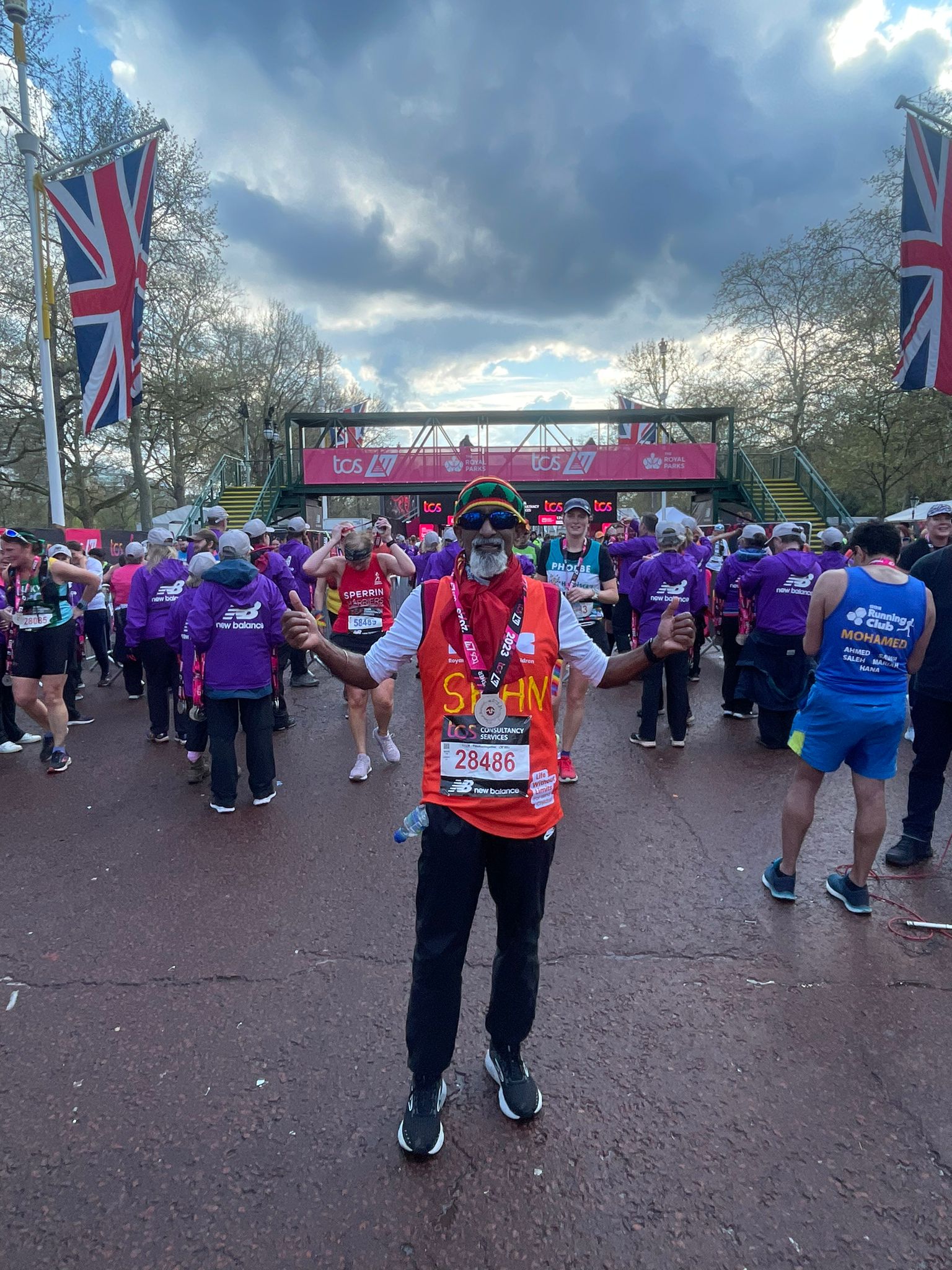 A man in the crowd at the finish line wearing the RSBC orange vest and with his arms up