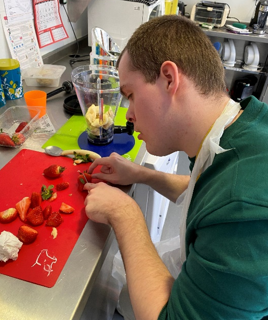 A young man chopping strawberries in a kitchen
