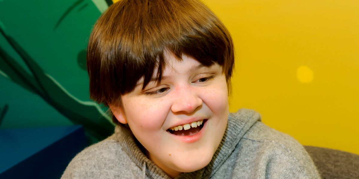 A vision impaired young person smiling in front of a multicoloured wall.
