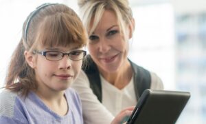 A vision impaired 7th year girl, wearing glasses and sat next to a female tutor.