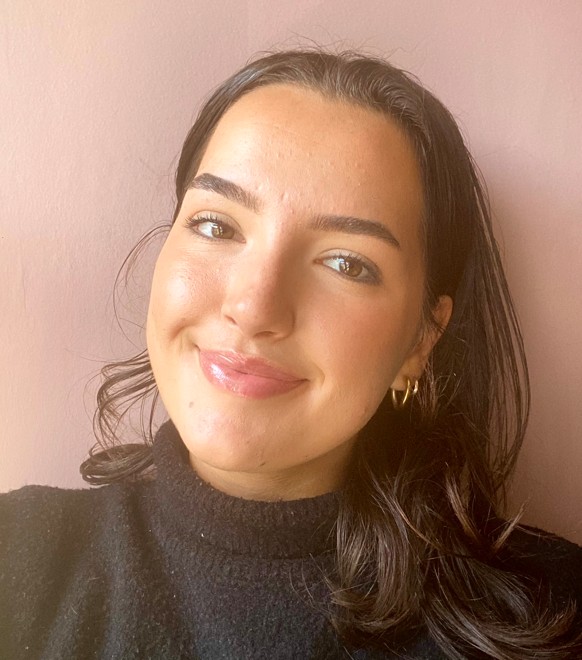 Isabella, a light-skinned women smiling directly at the camera with her head tilted slightly to the right. She has brown hair and is wearing a black turtle-neck jumper.